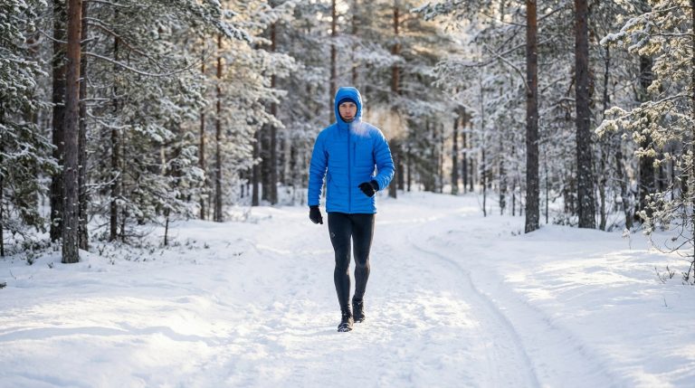 Gender-neutral figure in blue winter gear power walks on a snow path in a serene forest, breath visible in crisp air.